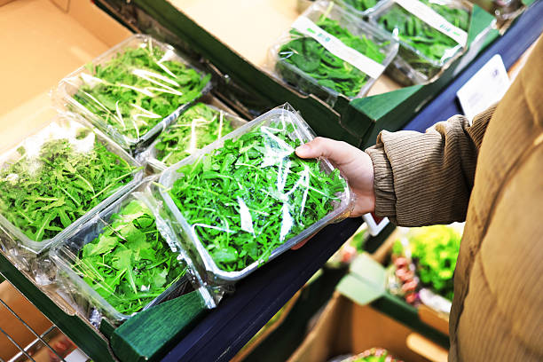 istock A person's hand selects a clear plastic container of fresh green arugula leaves from a refrigerated shelf in a grocery store 2246499418