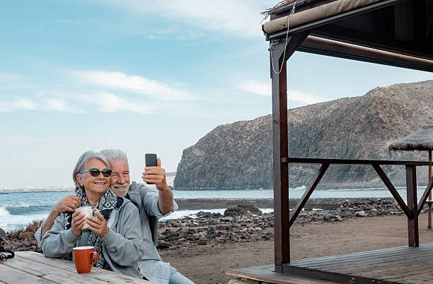 istock Smilling senior couple sitting for a break with a cup of tea along the seacoast while using smartphone for a selfie. Serene retirement lifestyle 2246500622