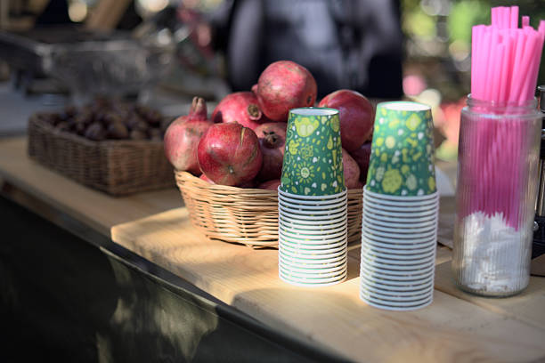 A market stall with pomegranates, paper cups, and straws.