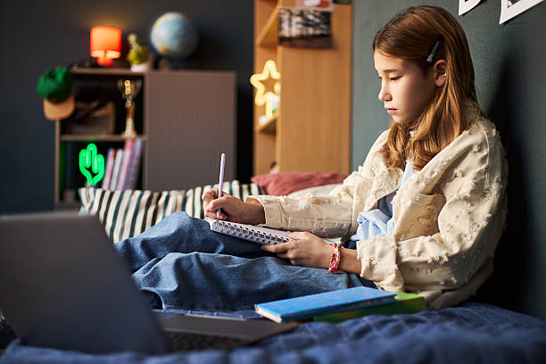 istock Teenage Caucasian Girl Sitting on Bed Writing in Notebook While Studying 2246502554