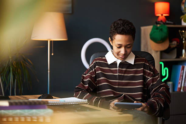 istock Teenage Black Boy Sitting at Desk Using Tablet in Modern Home Office 2246503112