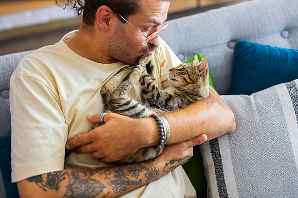 istock Relaxed man sitting on the sofa at home while gently petting his cat 2246509220