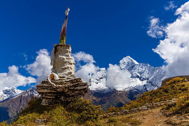 Traditional white-washed stupa and colourful Buddhist prayer flags fluttering in the thin mountain air above the Khumbu valley overlooked by Ama Dablam (6812m) deep in the remote Himalayan wilderness of the Sagarmatha National Park, a UNESCO World Heritage Site, Nepal.