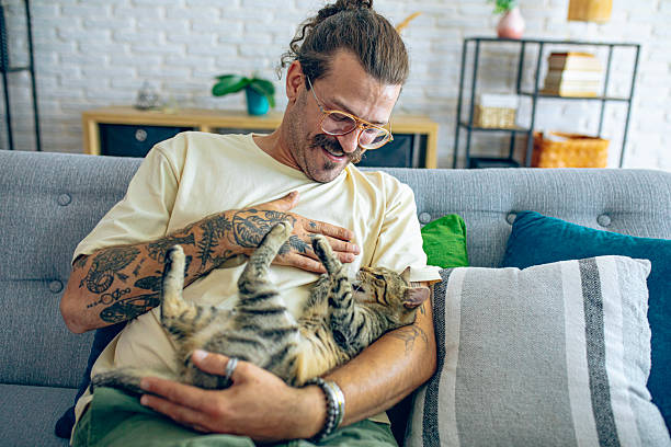 istock Relaxed man sitting on the sofa at home while gently petting his cat 2246509410
