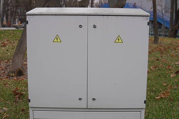 istock White Outdoor Electrical Control Box or Power Cabinet with Warning Stickers in Park Setting 2246512344