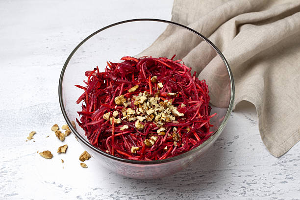 Healthy beetroot salad with shredded carrot, celery, onion, and chopped walnuts in a glass bowl on light textured background. Fresh vegetarian dish, close-up, with copy space for text or design