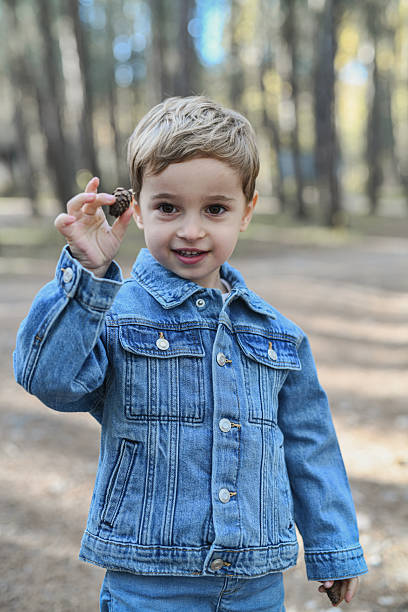 istock Young Boy In Denim Jacket Holding Pinecone In Forest Outdoors – Bright Smiles And Nature 2246516130