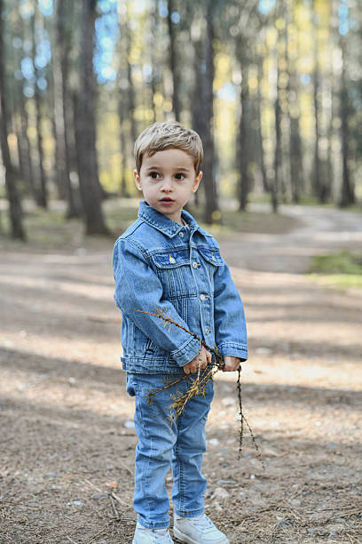 istock Young Boy in Denim Jacket Standing on Forest Path with Branches in Hands 2246516157