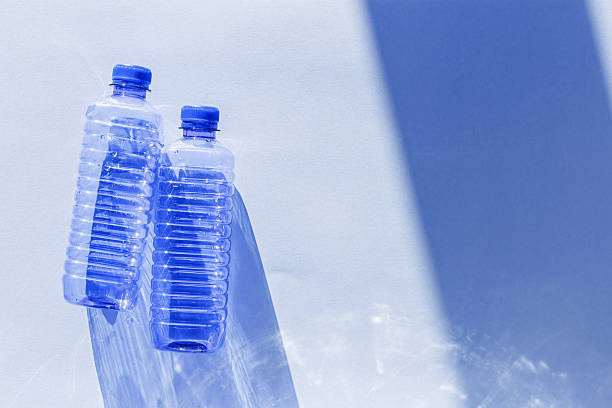 istock Transparent plastic bottles with blue caps and sun shadows on light background. Top view Water bottles at natural light. Themes of recycling, sustainability, water conservation, minimal style 2246518345