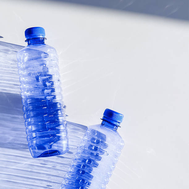istock Clear plastic water bottles for clean water on white blue background closeup, minimal aesthetic lifestyle photo, top view, flat lay, Naural light, sunlight shadows, caustic light effect, star filter 2246518351