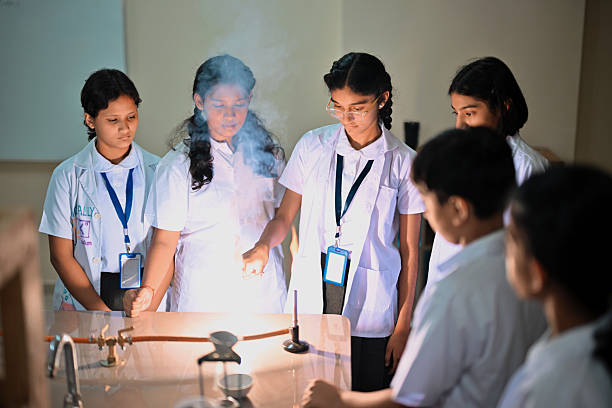 Middle school students in lab coats gather around a Bunsen burner as a bright flame and smoke rise during a flame test demonstration. The group watches closely, practicing basic lab safety and collaborative learning. Perfect for themes of STEM education, chemistry experiments, curiosity, teamwork, and classroom science activities.