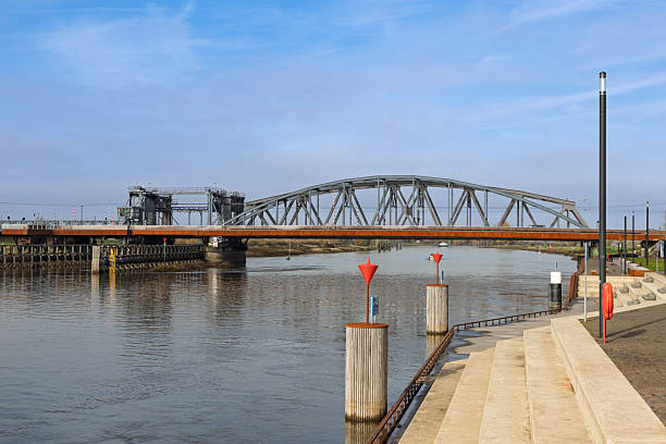 Wide view of the Oude IJsselbrug, a massive steel truss bridge over the wide IJssel river, with modern waterfront steps in Zutphen.