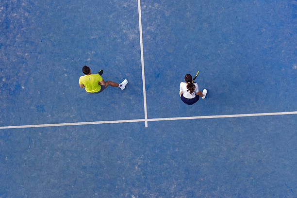 High-angle drone perspective of a man and woman in mid-play on a padel court. Represents athleticism, equality, and outdoor sports culture.