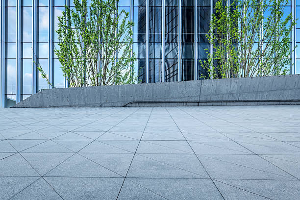 istock Empty square floor in front of a modern glass office building facade with green trees on a sunny day. 2246522874