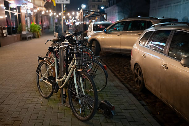 Secure bicycle parking setup with metal locking station on paved sidewalk near closely parked vehicles and commercial building lighting, illustrating practical urban mobility organization at night