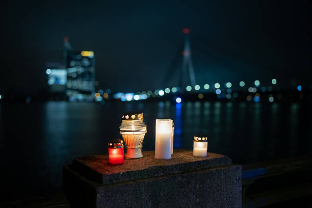 Warm candlelight placed on a stone surface overlooking the Latvian waterfront, with distant city architecture and bridge illumination forming a calm night backdrop that contrasts soft flame glow and urban reflections
