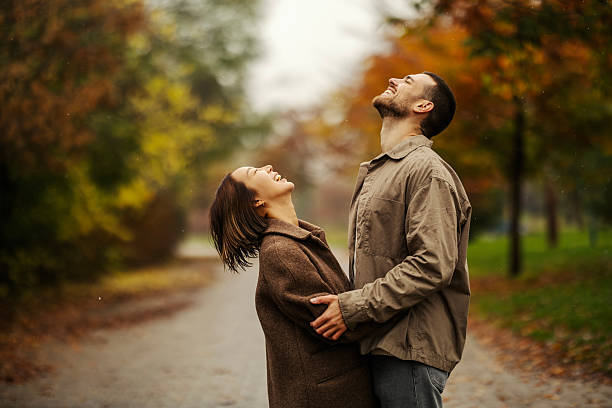 Cheerful couple embracing outdoors, feeling joy and refreshing rain in an autumn park. Celebrating love and togetherness
