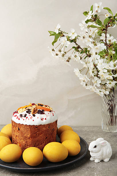 Traditional easter cakes with colorful sprinkles, with eggs, a bunny figurine, and spring flowers on grey concrete. Vertical photo