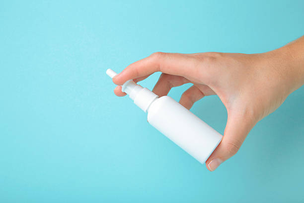 Hand holds a bottle of nasal drops on blue background. Top view