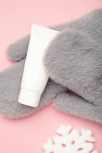 Winter skincare concept with grey mitten and moisturizing cream, surrounded by soft snow. Top view
