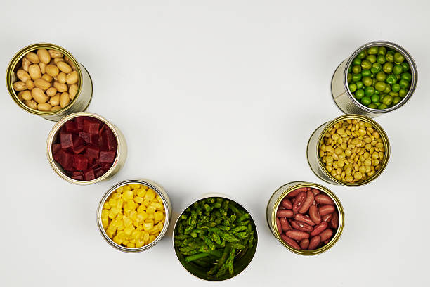 Open cans of beans, mushrooms, carrots, corn, peas, green beans, lentils, asparagus, and olives on a white background with copy space.