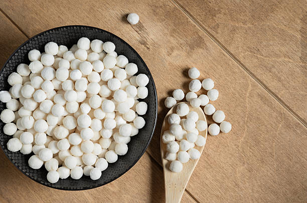 istock Organic tapioca pearls in black bowl on wooden table top view. Spoon with white dry tapioca pearls, cooking ingredient, gluten-free food, healthy eating. 2246535159