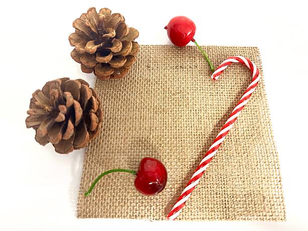 Rustic holiday decorations featuring pine cones, shiny cherries, candy cane, and burlap background for festive celebrations and seasonal aesthetics