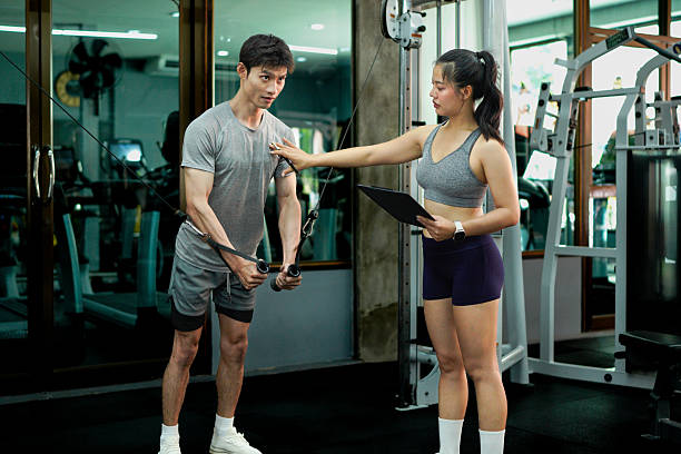 istock Young man in gym with his personal trainer working out on cable weight machine. 2246537173