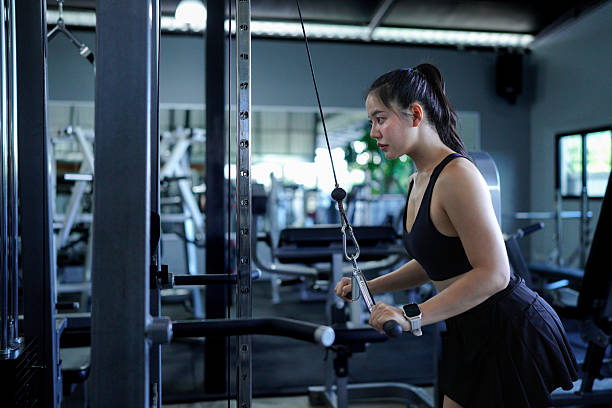 istock Fit Asian woman pulling down weights on a cable machine at the gym, training her biceps and building muscle strength. fitness center health workout concept 2246537287