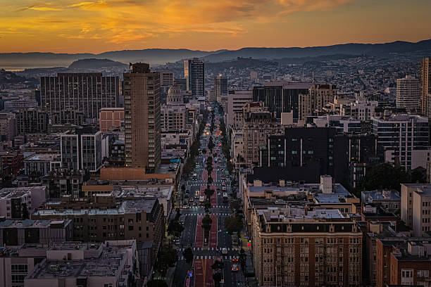 An aerial view looking down Van Ness in San Francisco at sunrise. Buildings and vehicles illuminated against the dramatic sunrise.