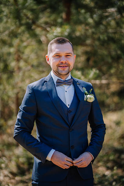 istock Stylish man in a formal suit with a bow tie stands confidently outdoors, surrounded by greenery, showcasing elegance and sophistication in a natural setting 2246540733