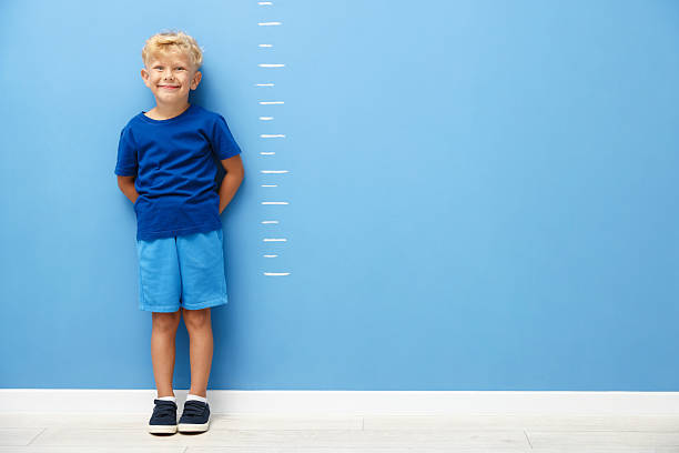 istock Cute little boy measuring his height near blue wall. Space for text 2246541038