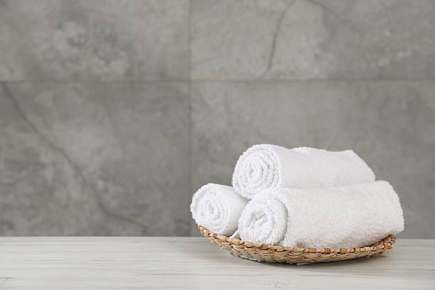 istock Rolled towels on light wooden table against grey wall, closeup. Space for text 2246543127