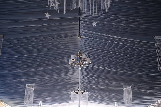 Chandelier hangs gracefully beneath a draped fabric ceiling adorned with delicate star decorations creating an elegant and festive atmosphere perfect for weddings galas or any special celebration.