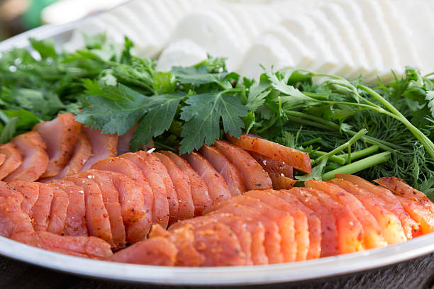 A close-up of a beautifully arranged plate featuring thinly sliced smoked fish, a generous pile of fresh parsley and dill, and round slices of white cheese in the background. The vibrant greens and reds create an inviting display, perfect for a fresh appetizer or a festive table setting.