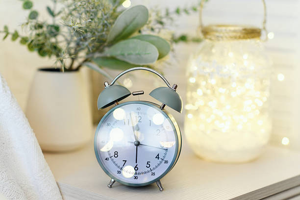 istock Alarm clock standing on nightstand near bed with small christmas tree and light lamp with garland. Christmas, New year concept. 2246550476
