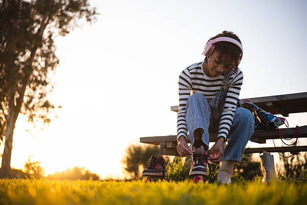 Young woman wearing headphones and tying roller skates on a picnic table during sunset