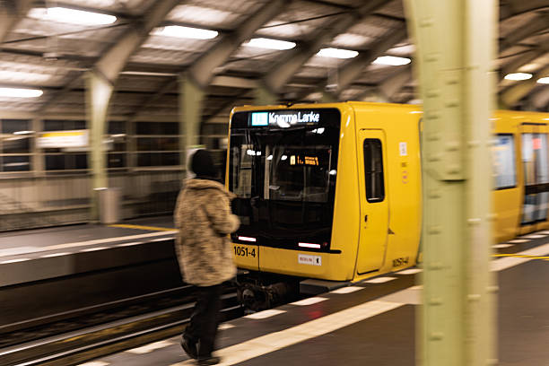Berlin, Germany – November 11, 2025: A BVG U-Bahn train arrives at a Berlin station platform as a commuter approaches the edge of the platform. The scene shows nighttime metro service with motion blur from the moving train.