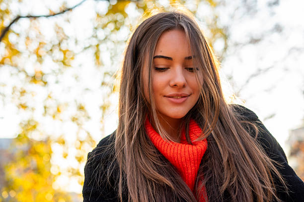 Young adult woman with long hair smiling at park during fall