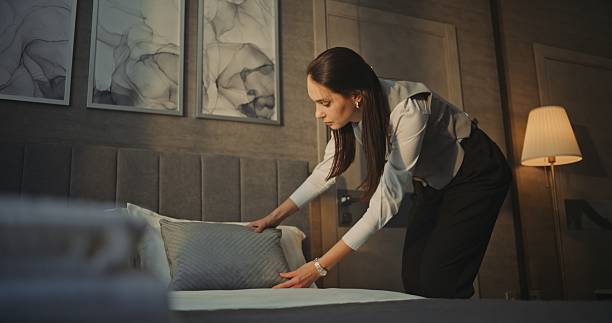 istock Housekeeping Woman Employee in Uniform Adjusts Bedding and Pillow Placement 2246566840