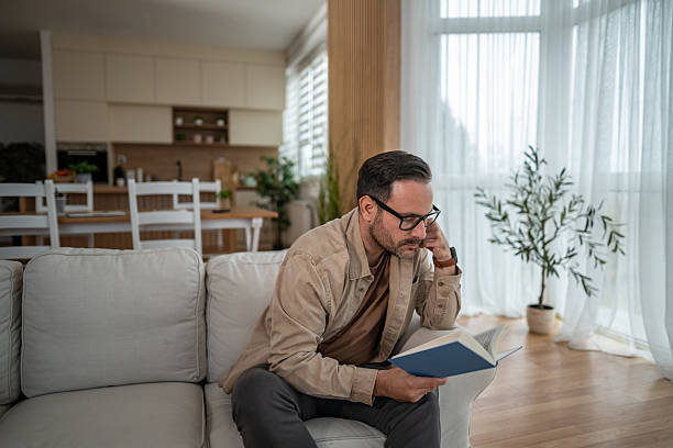 istock Man reading book on couch in modern home 2246570392