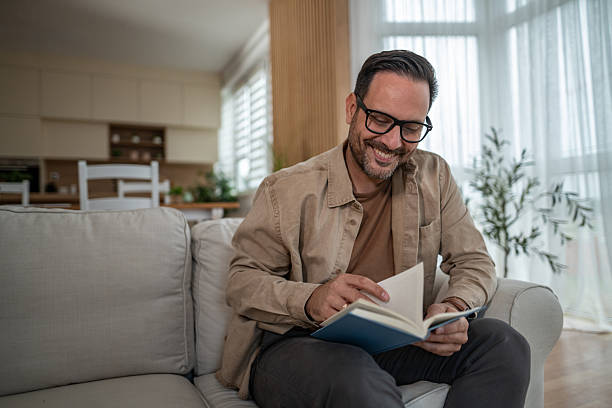 istock Happy man relaxing on couch reading book at home 2246570407