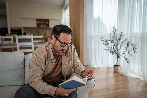 istock Man relaxing at home reading book on couch 2246570412