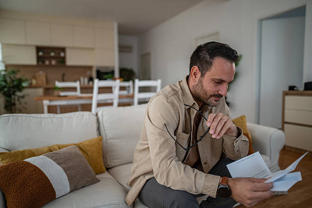 istock Man reading financial mail at home on couch 2246572516