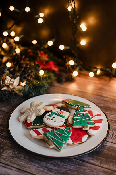 istock Christmas cookies on plate with golden lights on rustic table. Baking traditional snowman, tree, star cookies and santa hat for holidays 2246572519
