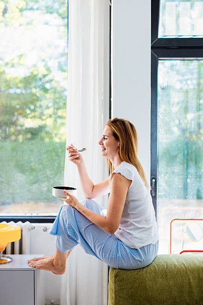 istock Relaxed Woman Eating Breakfast While Sitting by Large Window in Bright Home Interior 2246578486