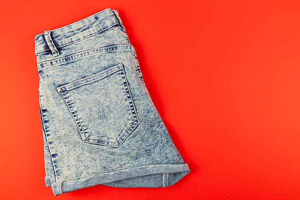 istock Stylish folded denim shorts on a bright red background 2246578706