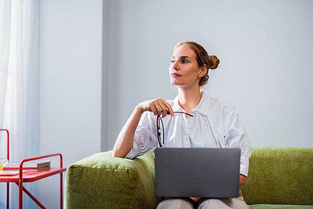 istock Thoughtful Woman With Laptop Sitting On Green Sofa In Modern Home Office Setting 2246578779