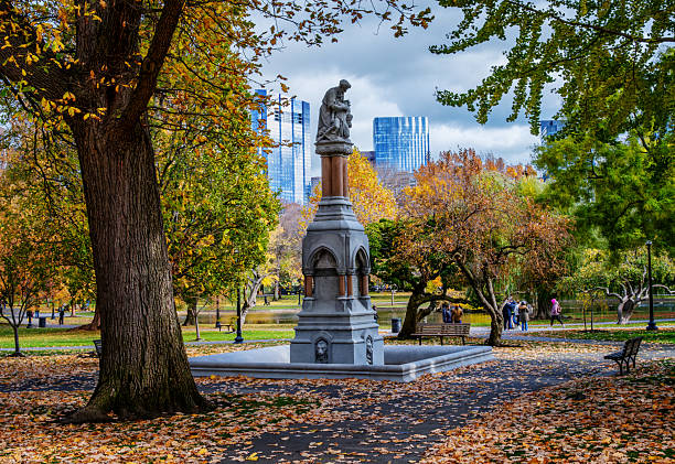 Boston, Massachusetts, USA - November 11, 2025: The Ether Monument, located towards the corner of Arlington and Beacon streets in the northwest corner of the garden, commemorates the first use of ether as an anesthetic. Designed by John Quincy Adams Ward and gifted to the city in  1868, by Thomas Lee, it is the oldest monument in the garden. Standing 30 feet tall and made of granite and red marble, the statue's carved figures tell the Parable of the Good Samaritan. Established in 1837, the Public Garden is a large park in the heart of Boston, adjacent to Boston Common. It is a part of the Emerald Necklace system of parks. The Public Garden was the first public botanical garden in America and here it is displaying its autumn colors.