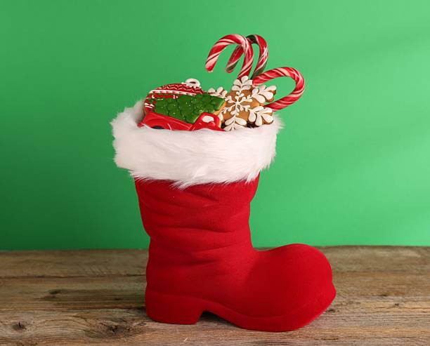 istock Saint Nicholas day tradition. Red boot with sweets on wooden table against green background 2246583124